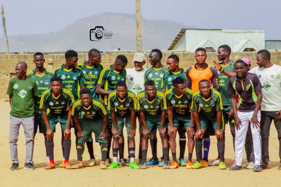 Coordinators of Music Plus Football pose with players from one of the teams on a community football pitch.
