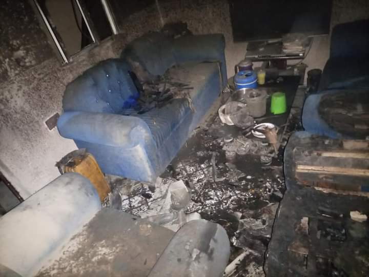 A charred room with burnt furniture and debris after a fire incident.