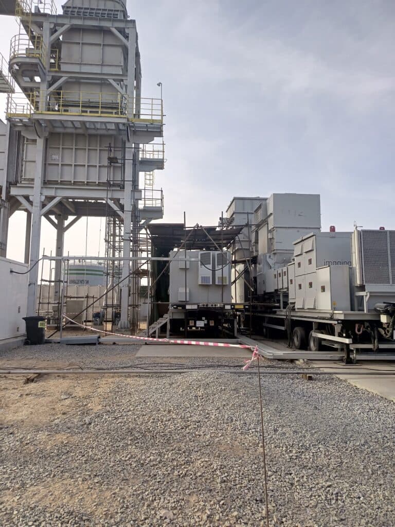 Industrial scene with a large transformer being transported on a trailer near electrical infrastructure.
