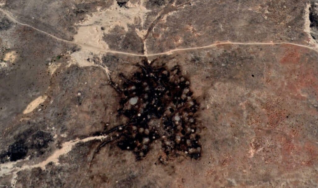 Aerial view of a landscape with a centralized explosion mark and radiating trails on the ground.