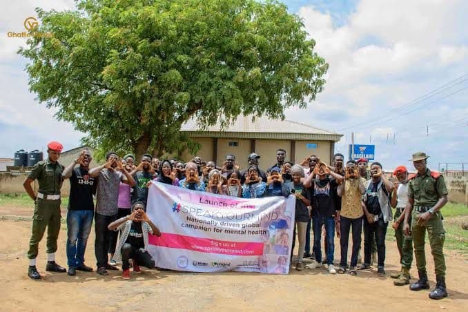 Group of people posing with a banner for the launch of a mental health campaign, making hand gestures to signify unity.