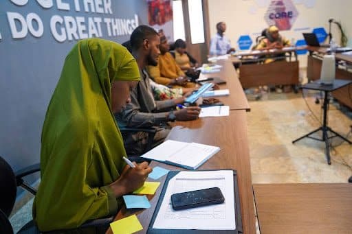 Students seated in a row at a seminar, taking notes, with a motivational "TOGETHER WE DO GREAT THINGS!" banner in the background.