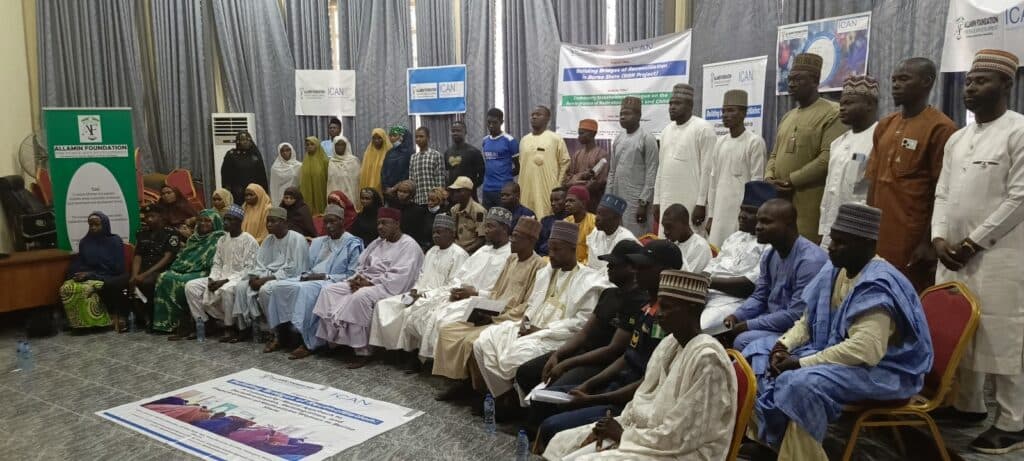 Group of individuals in traditional attire at an indoor reconciliation event with banners and posters.