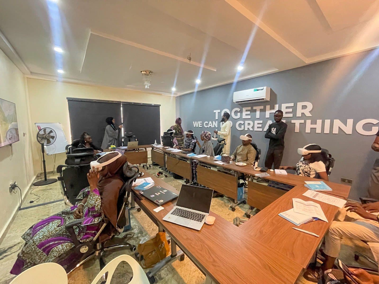 Group of people engaged in a meeting or training session in an office with the slogan "Together we can do great things" on the wall.