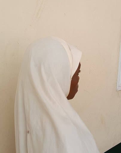 Profile of a person in a white hijab against a textured wall.