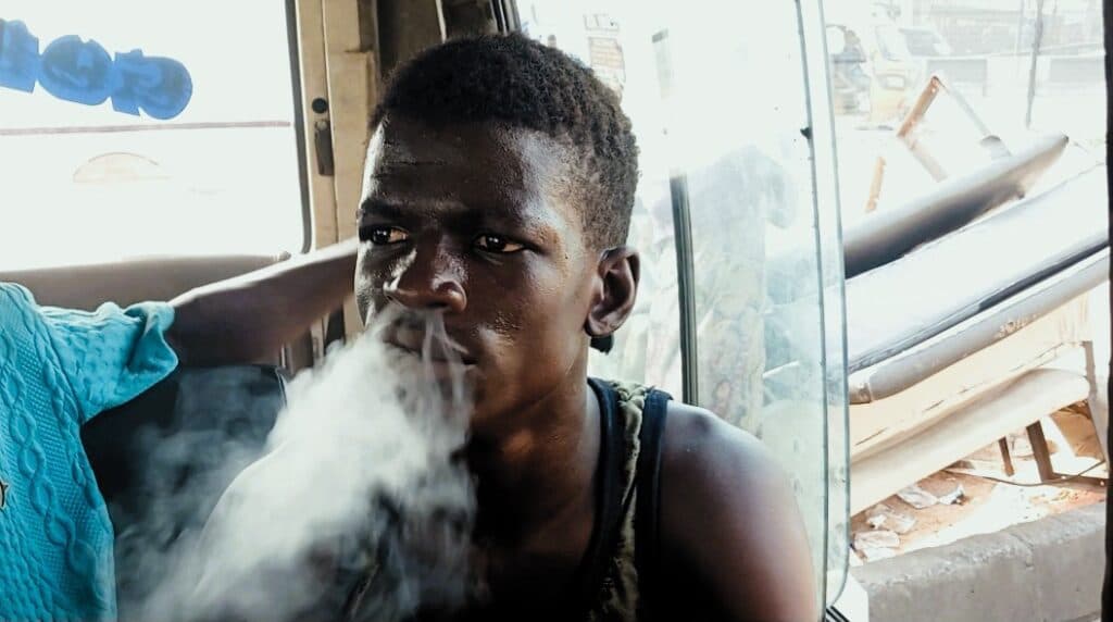 Young man exhaling smoke while sitting inside a vehicle, with a thoughtful expression.