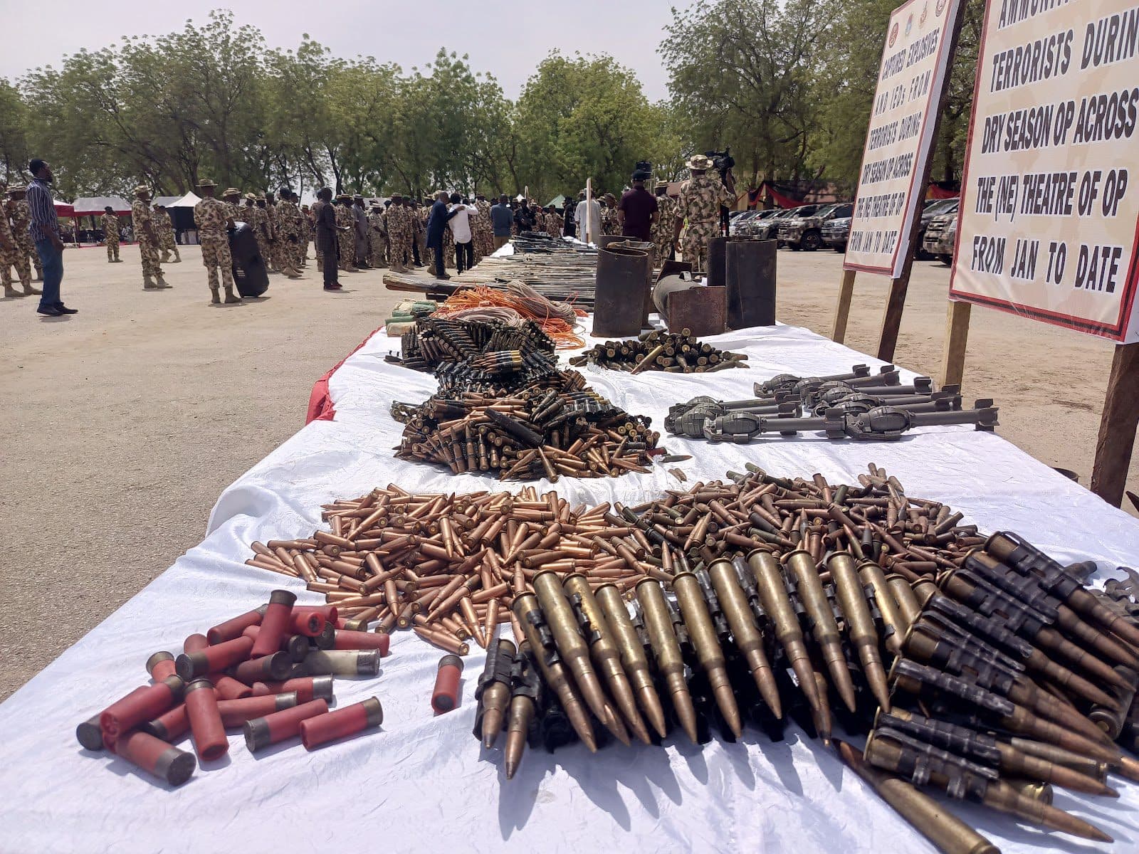 Table with seized ammunition and weapons on display, military personnel in background, outdoors under daylight.