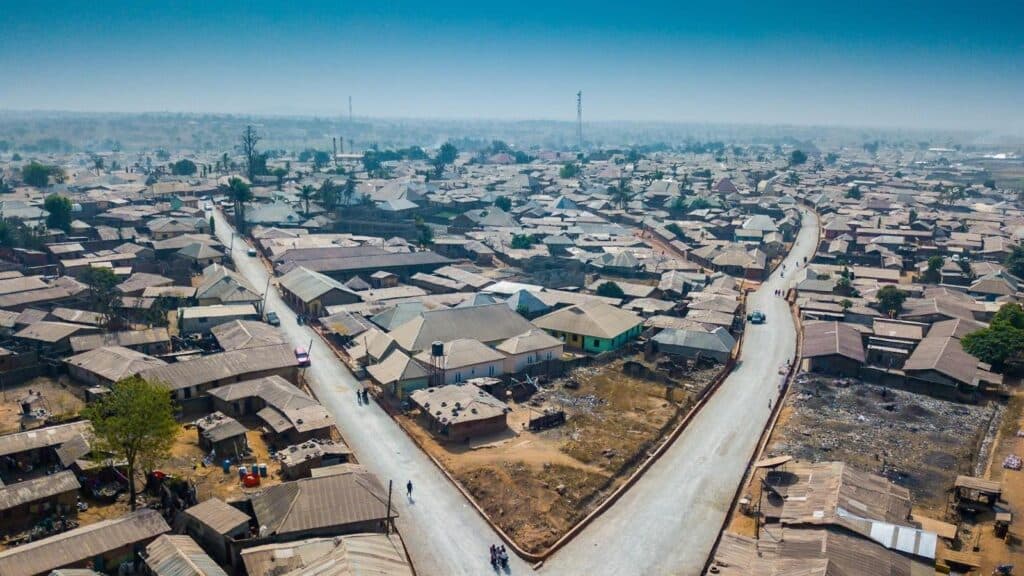 Aerial view of a dense settlement with tin roofs along a winding road.