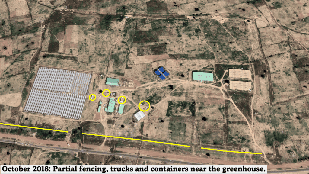 Aerial view of a rural area with annotated features such as partial fencing, trucks, and containers near a greenhouse.