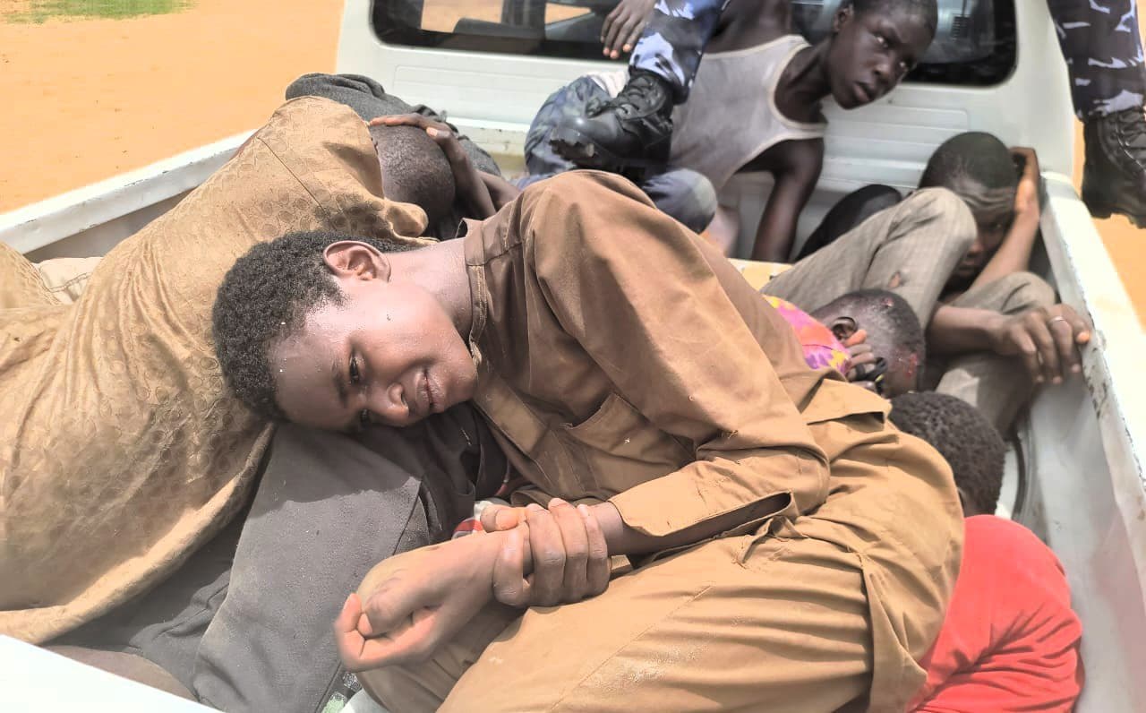 Several people lying in the back of a pickup truck, with a focus on one individual looking at the camera.