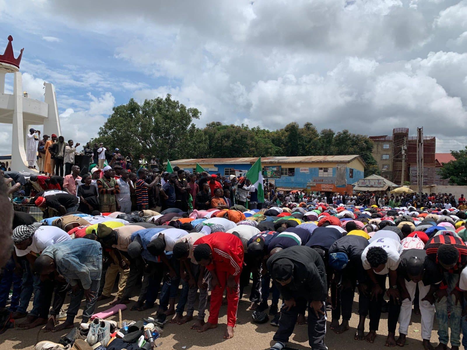 A crowd of people bowing down in prayer with some standing and waving a flag, possibly at a public gathering or demonstration.