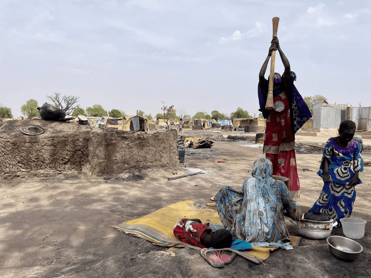 People amidst a makeshift environment with basic belongings, indicating a scene of daily life in a resource-scarce setting.