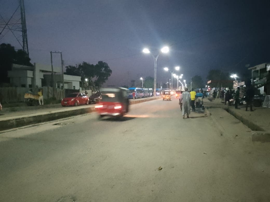 A busy street at twilight with pedestrians, vehicles, and street lighting.