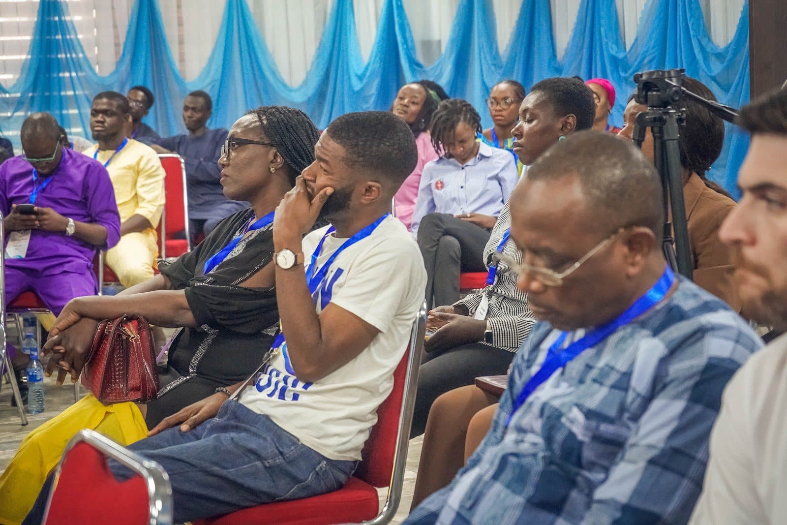 Audience members seated at an event with blue and white decor, focused on the presentation.