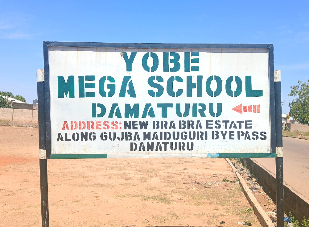 Sign for Yobe Mega School, Damaturu, with address: New Bra Bra Estate, along Gujba Maiduguri Bypass, Damaturu, under a clear sky.