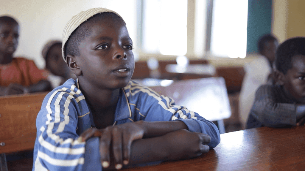 Young student in a classroom, focused and attentive, wearing a blue and white striped jacket.