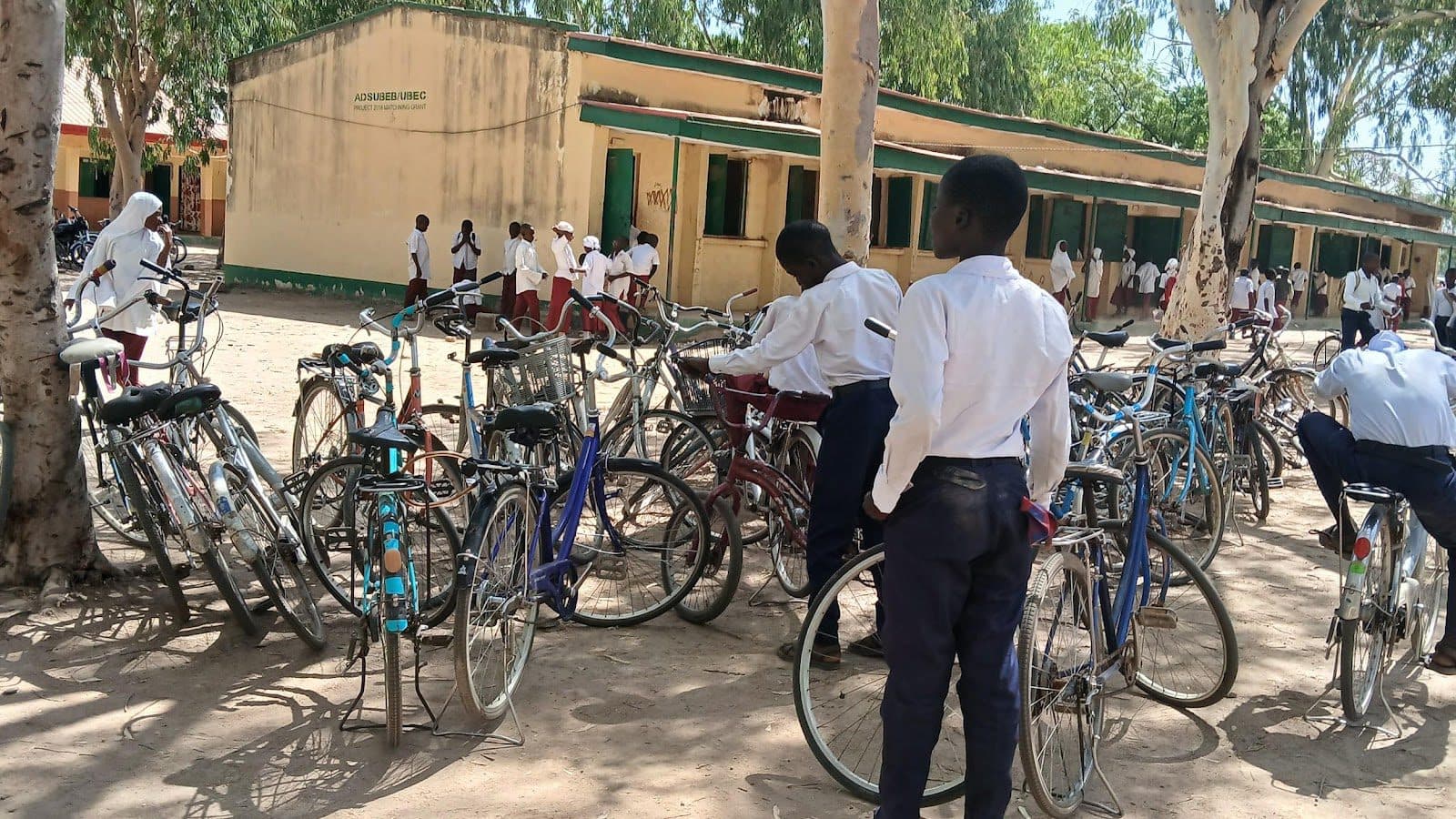 Students in uniform gather around bicycles outside a school building on a sunny day.