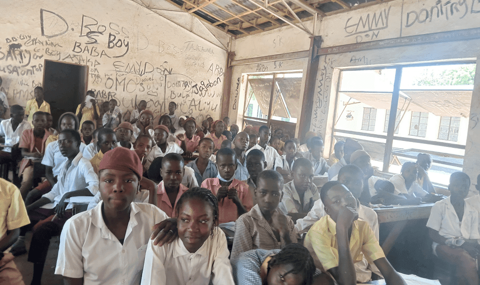 Classroom filled with students in uniforms, some smiling, some serious. The walls are covered with graffiti.