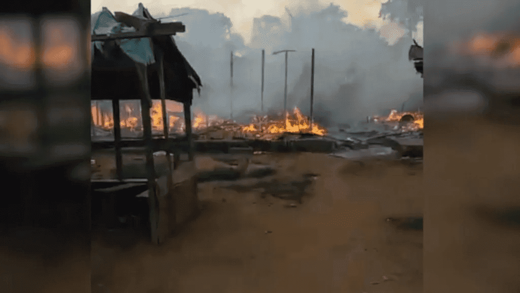 Burned structures smolder, with flames and smoke rising in a rural area, creating a scene of devastation.