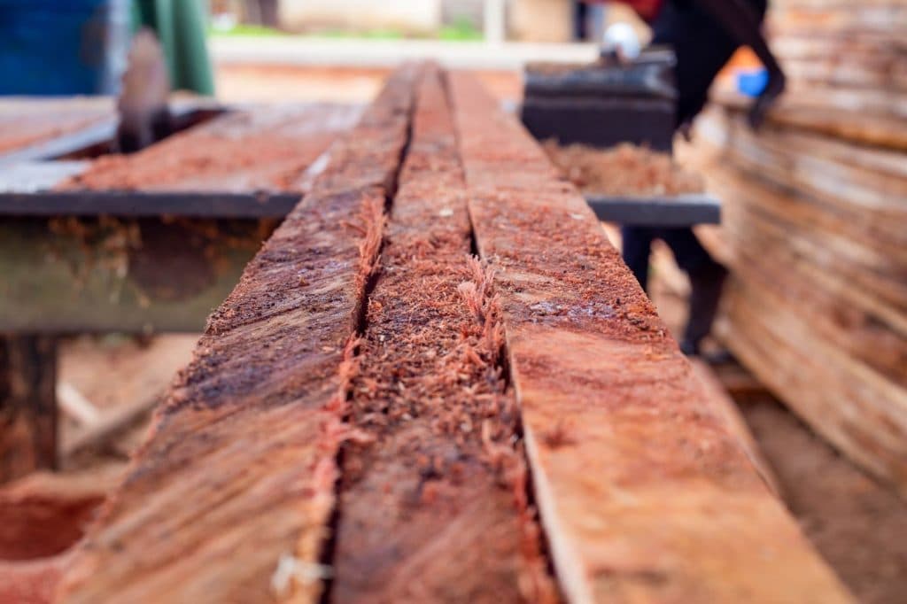 Close-up of a freshly cut wooden plank in a sawmill, with red sawdust scattered on top.