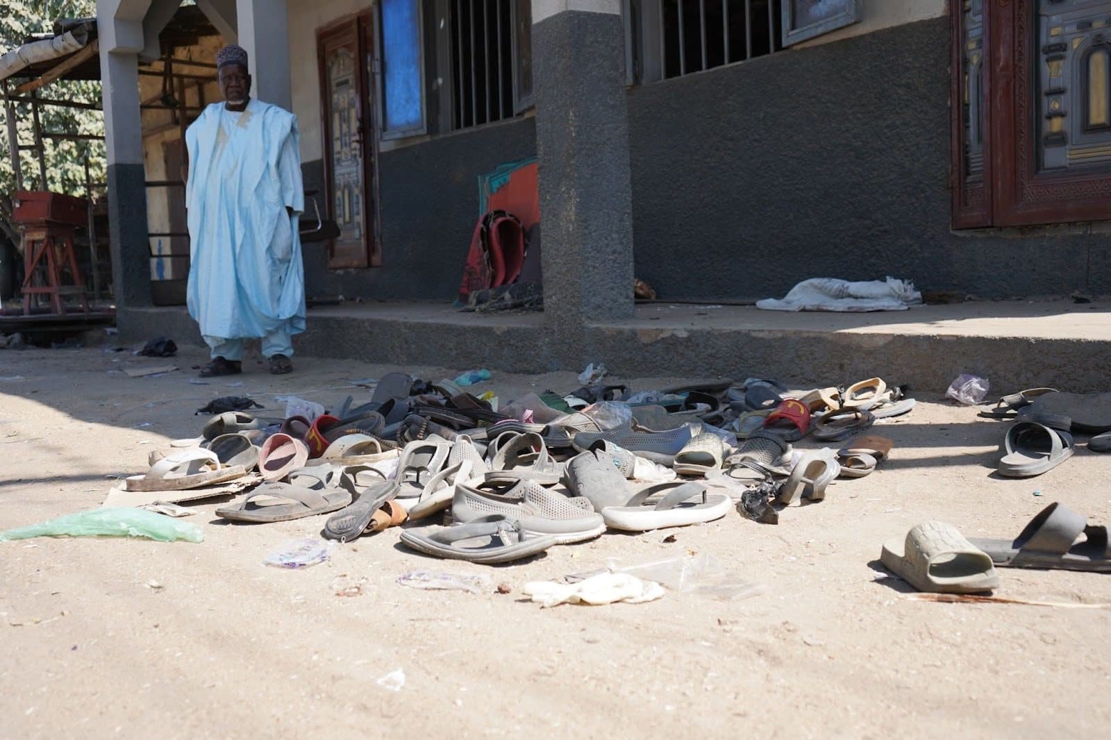 Sandals scattered on the ground outside a building with a person standing near the entrance.