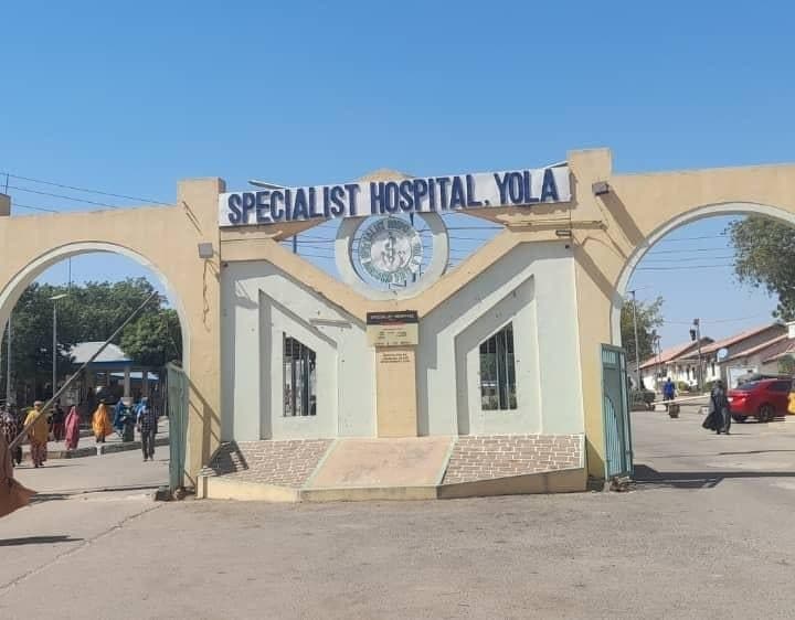 Entrance of Specialist Hospital Yola, featuring an archway and people walking nearby under a clear blue sky.