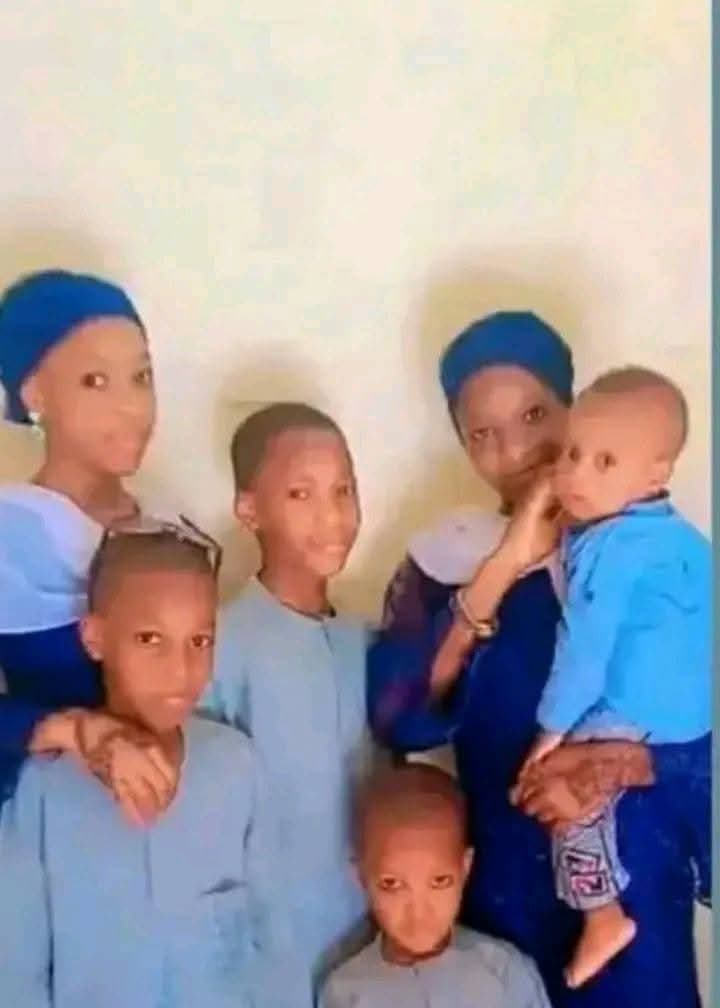 A group photo of six people, including four children and an adult holding a baby, all wearing matching blue outfits.