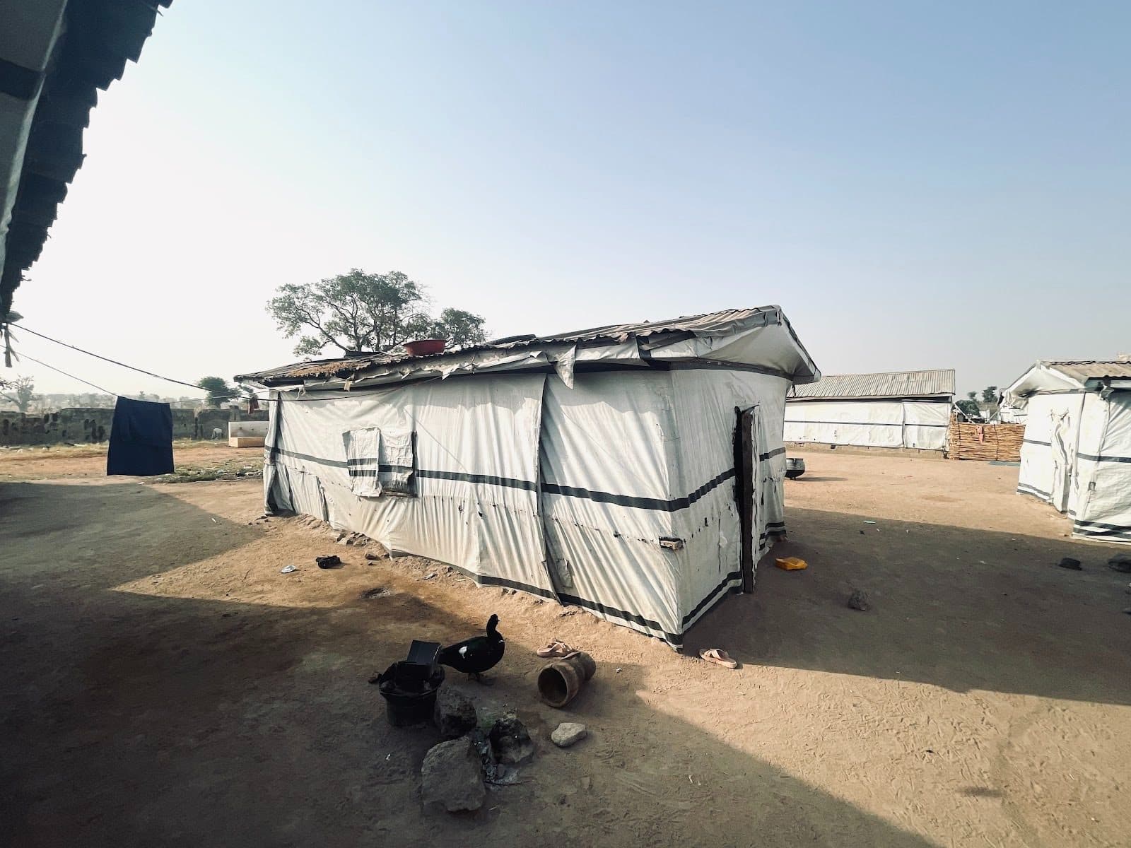Simple structures with tarpaulin walls in a dusty, open area under a clear sky.