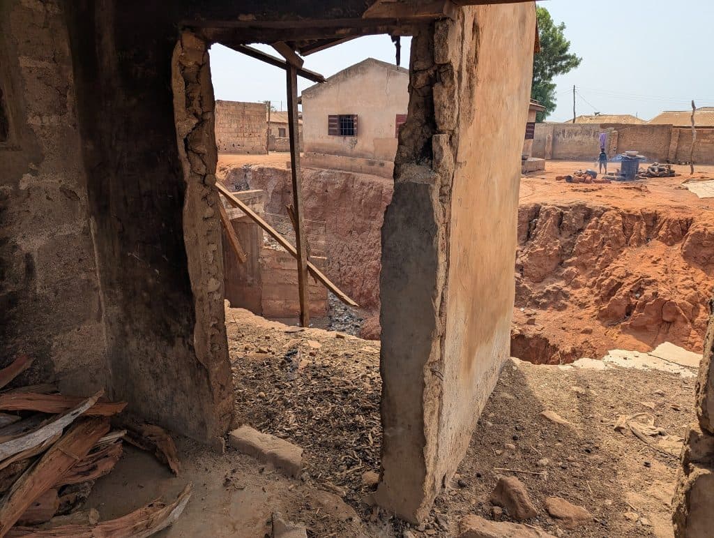 View through a crumbling doorway to a dusty, eroded landscape with buildings and a person in the distance.