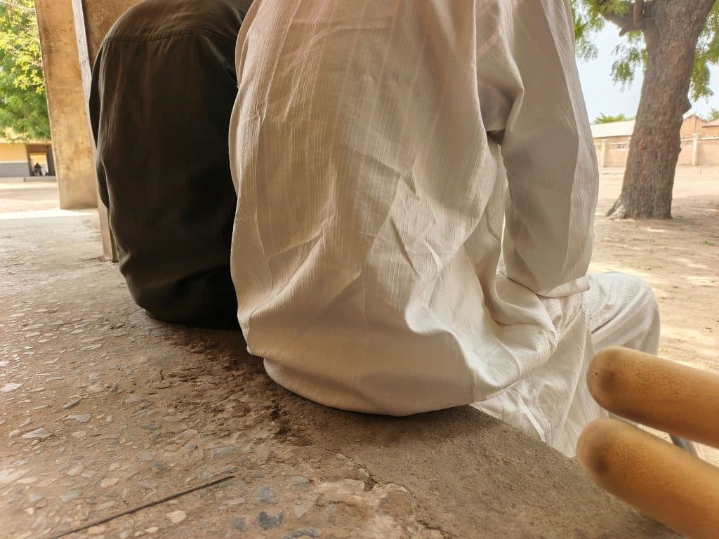 Two people sitting side by side on a ledge, one in brown and one in white. There