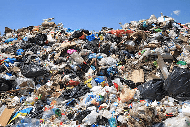 A large pile of assorted trash and plastic bags at a landfill under a clear blue sky.