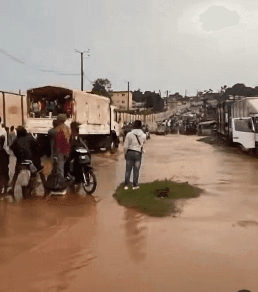 Flooded street with trucks, motorbike, and people navigating through water.
