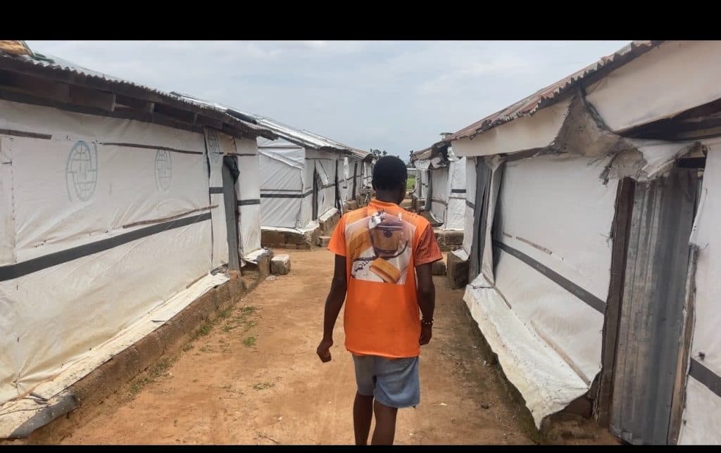 Person in an orange shirt walks down a path between white tents with metal roofs.