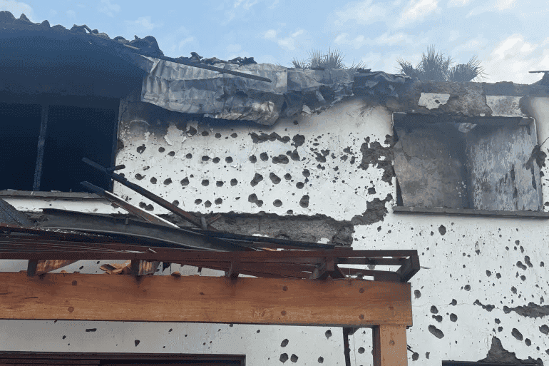 Damaged building with exterior walls covered in holes and debris from roof, under a partly cloudy sky.