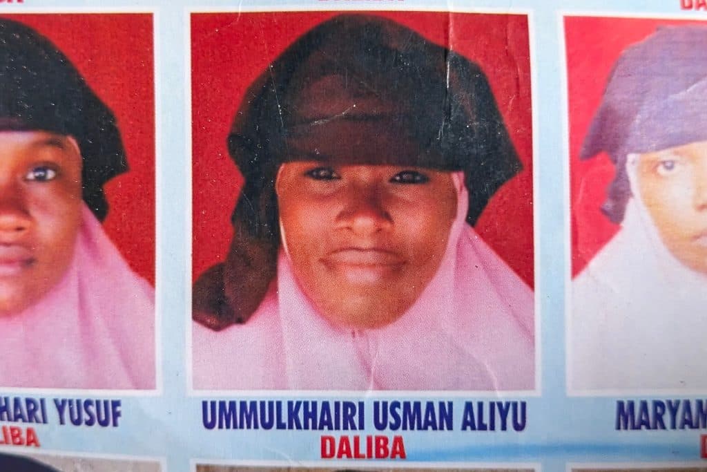 Headshot of a person wearing a hijab, with a red background, accompanied by text at the bottom.