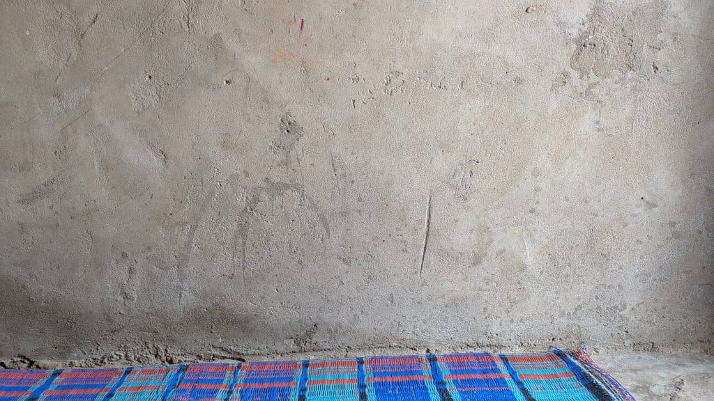 A textured beige wall with a woven blue and red mat partially visible at the bottom edge.