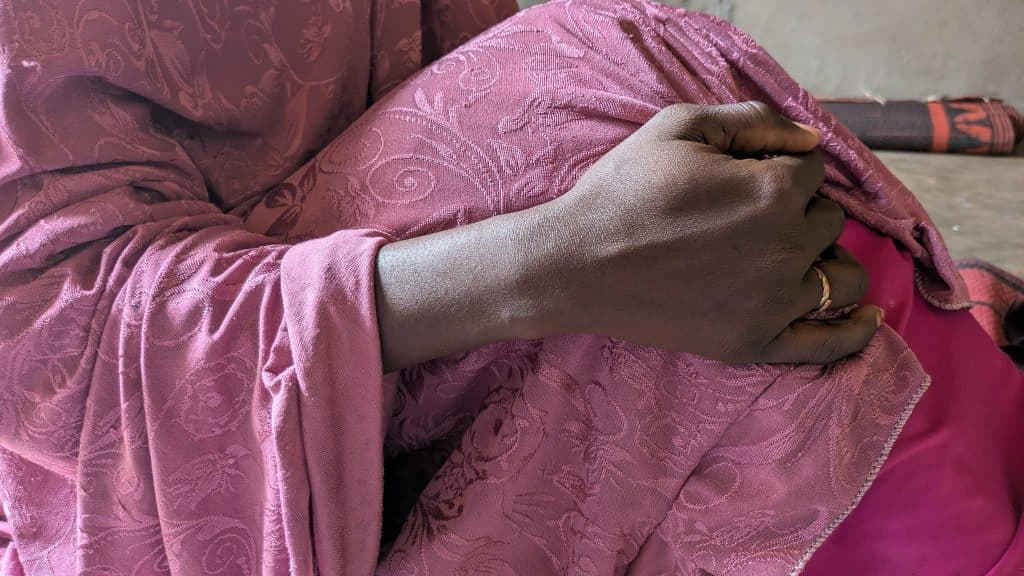 A person in a patterned pink fabric is holding the material close, showing a ring on their finger against the textured cloth.
