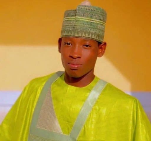Person wearing a green traditional outfit and matching hat, standing against an orange background.