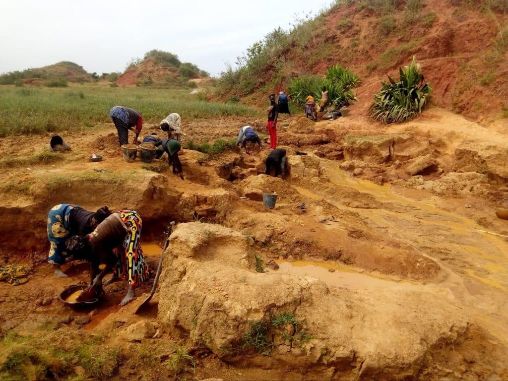 People working in a rural area, digging and sorting soil in a rugged landscape with hills and sparse vegetation around them.