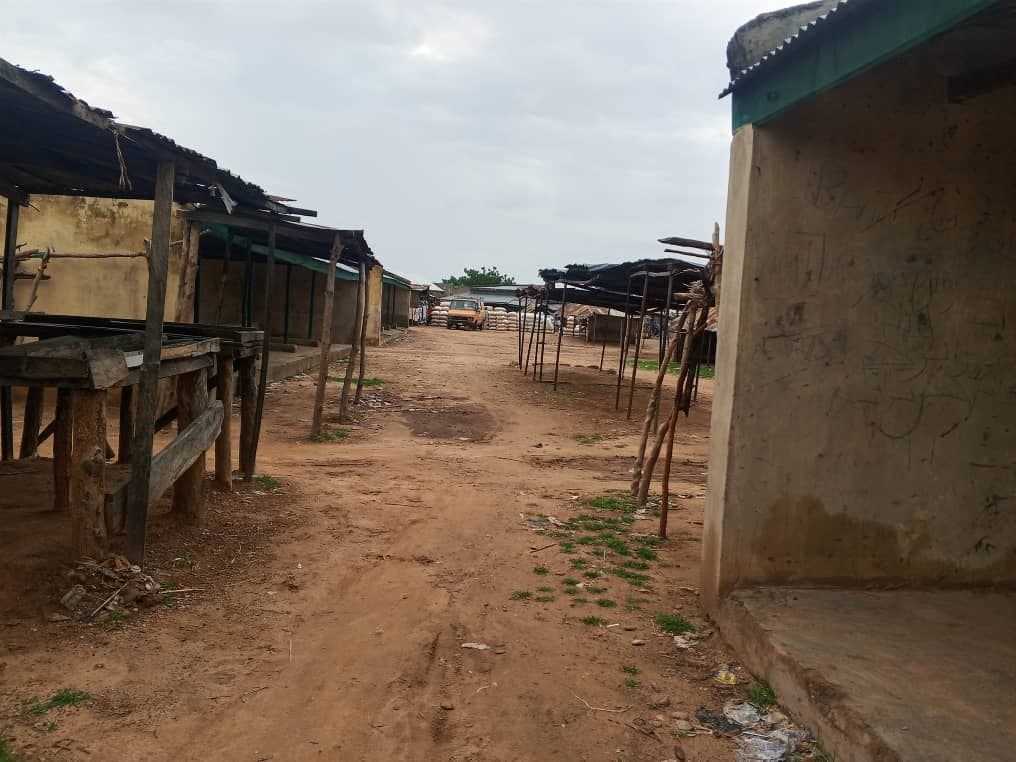Empty outdoor market with wooden stalls on a dirt path, under cloudy skies.