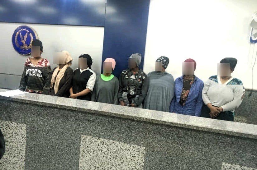 Group of people with obscured faces standing by a counter with an emblem on the wall behind them.