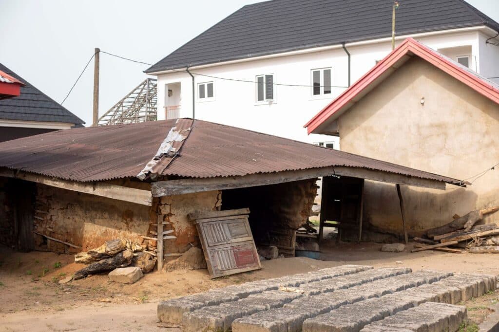 Dilapidated building with corrugated iron roof in front of modern houses.
