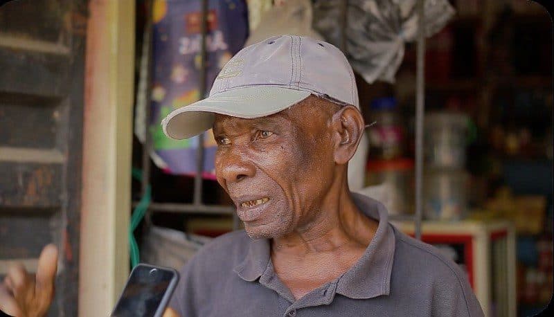 Elderly man in a cap holding a smartphone with a puzzled expression.