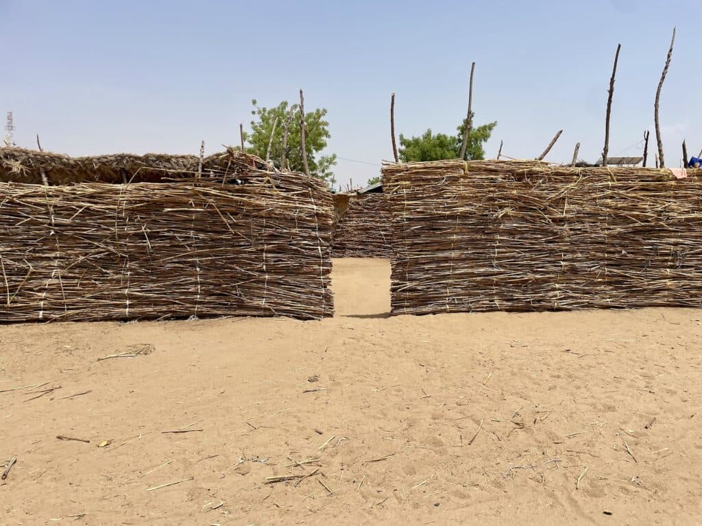 A traditional woven fence with a small doorway, under a clear blue sky.