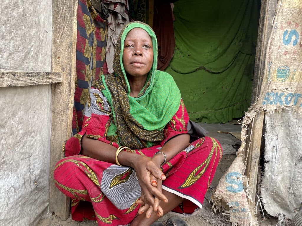 Woman in colorful attire sitting at a tent entrance.