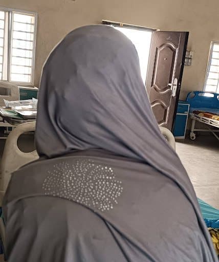 A person wearing a hijab with a rhinestone pattern, seen from behind in a room with hospital beds.