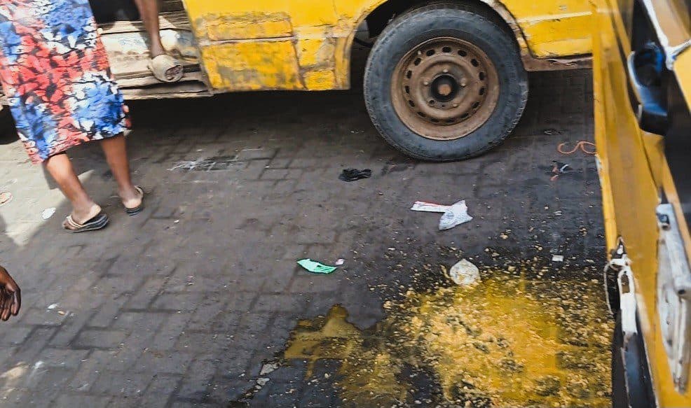 A bustling street scene with a person walking by a yellow bus, litter on the ground, and a puddle reflecting light.