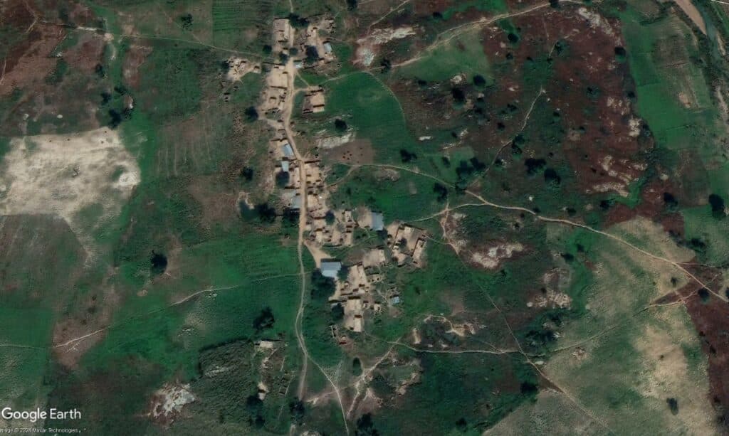 Aerial view of a rural village with scattered buildings amid green and brown fields.