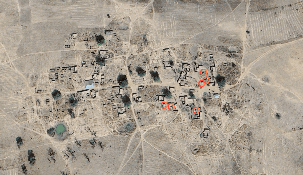 Aerial view of a rural area with scattered buildings and patches of vegetation, marked by red circles.