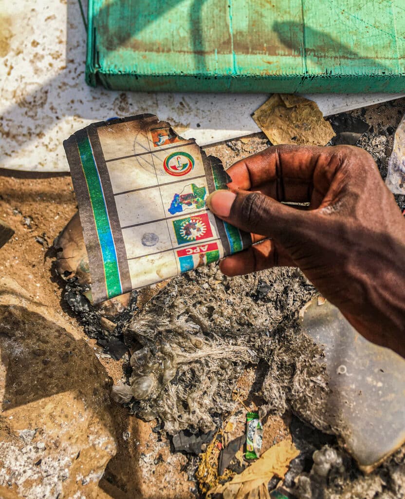 Hand holding a charred document among debris and ashes.